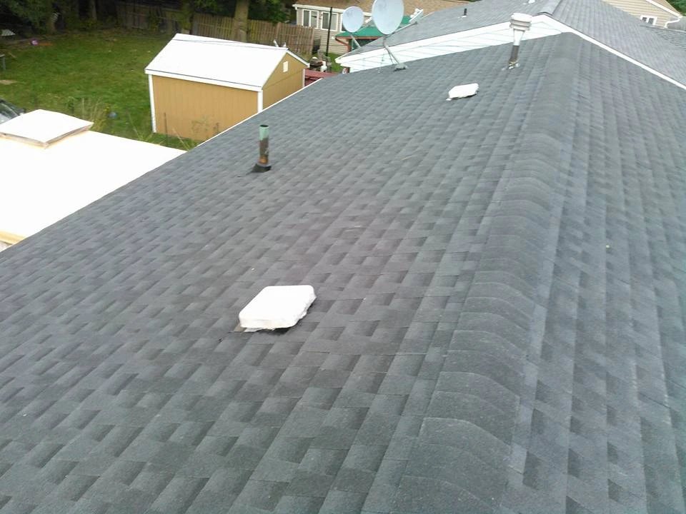 An expansive view of a new asphalt shingle roof with a neat pattern. Visible roof vents and skylights are installed, and the background features a shed and satellite dish, suggesting this is a residential home.